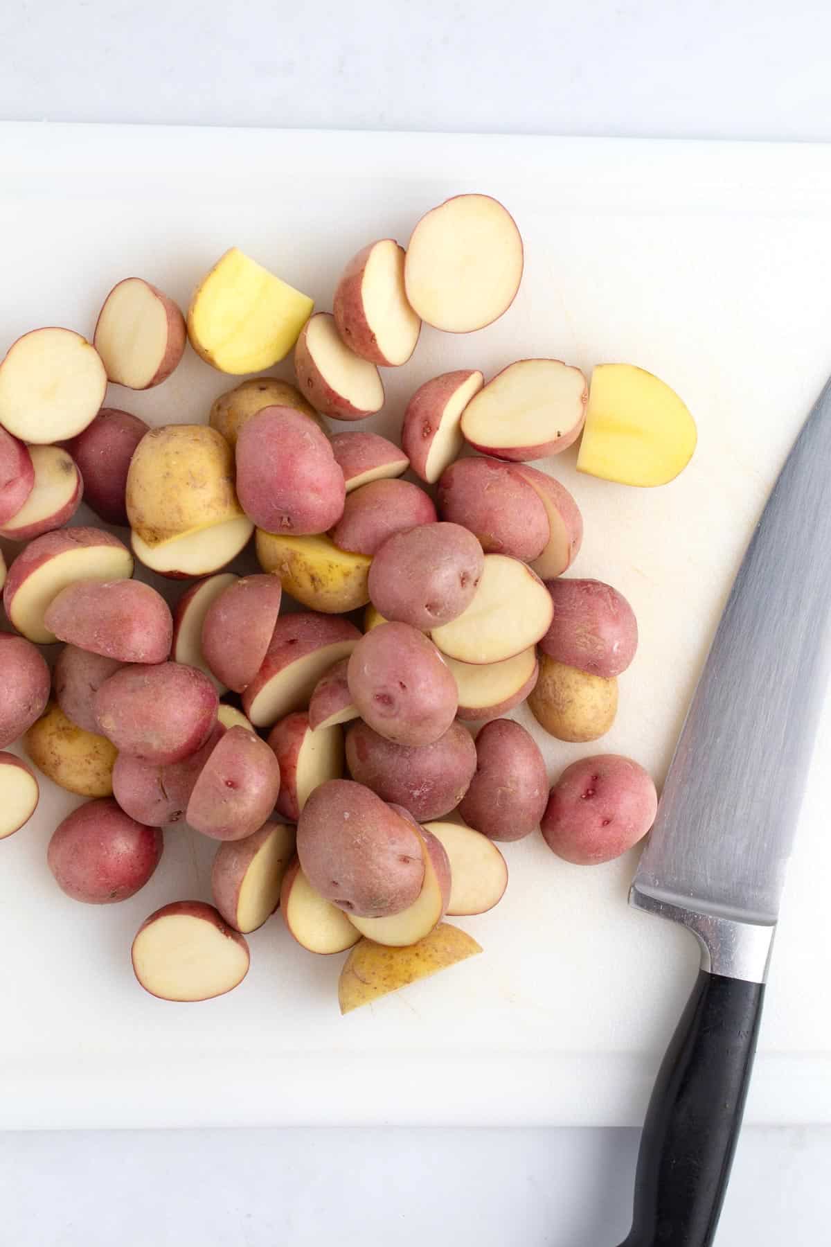 Small spuds cut in half on cutting board with knife.