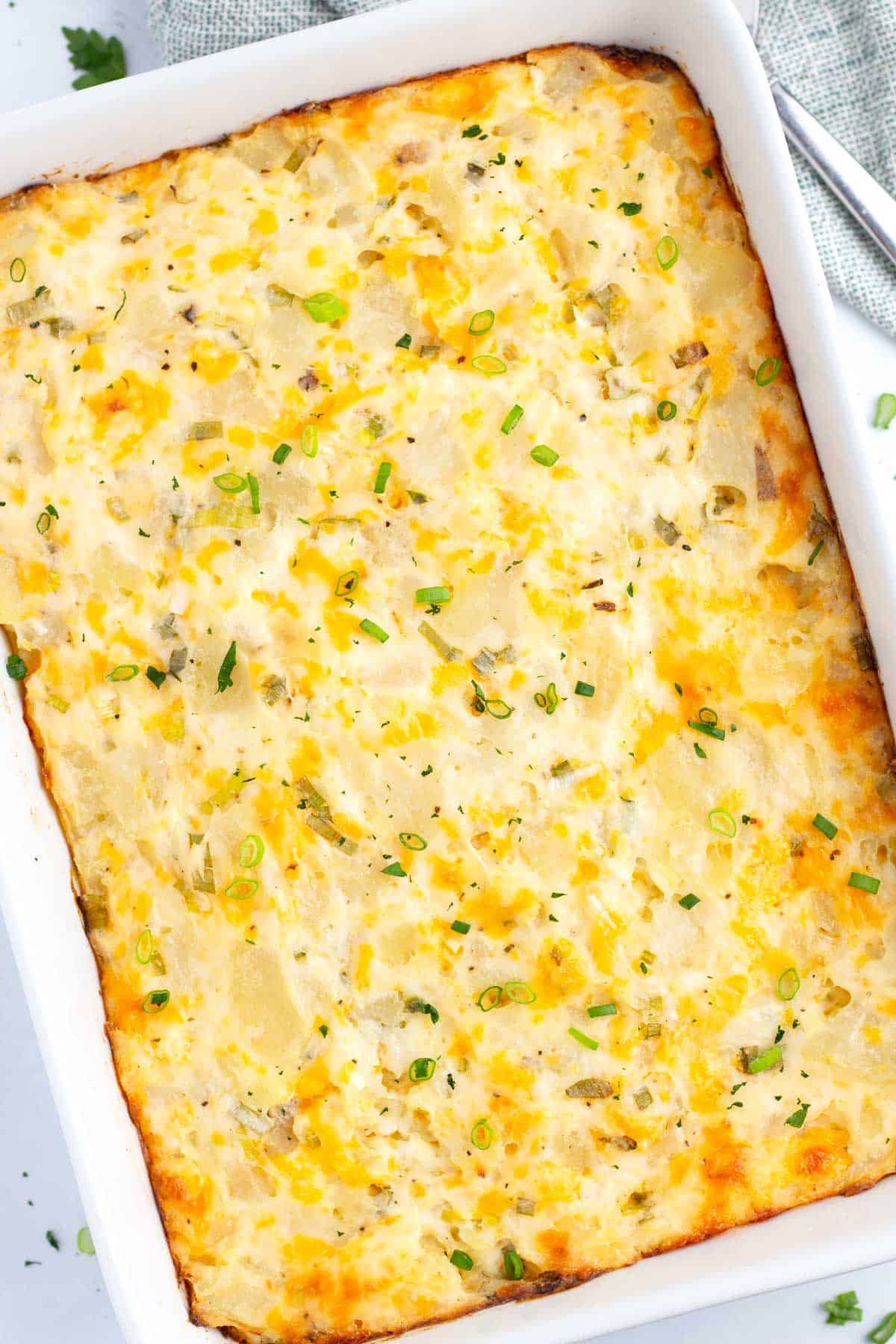 Baking dish filled with final potato casserole held together with sour cream, cheddar cheese, and green onions.