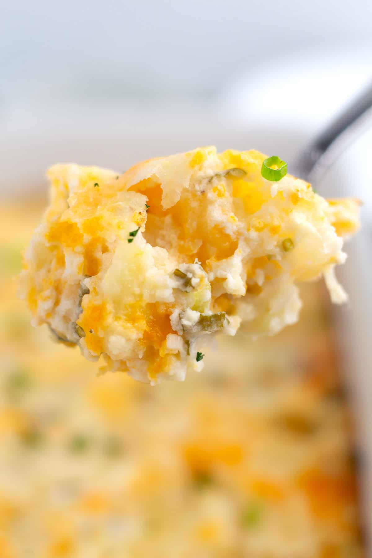 Spoonful of sour cream potato bake on a serving spoon sprinkled with chives.