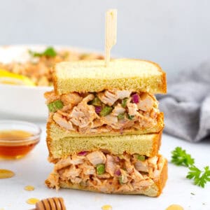 Soft sandwich bread filled with hot honey chicken salad with serving bowl in background.
