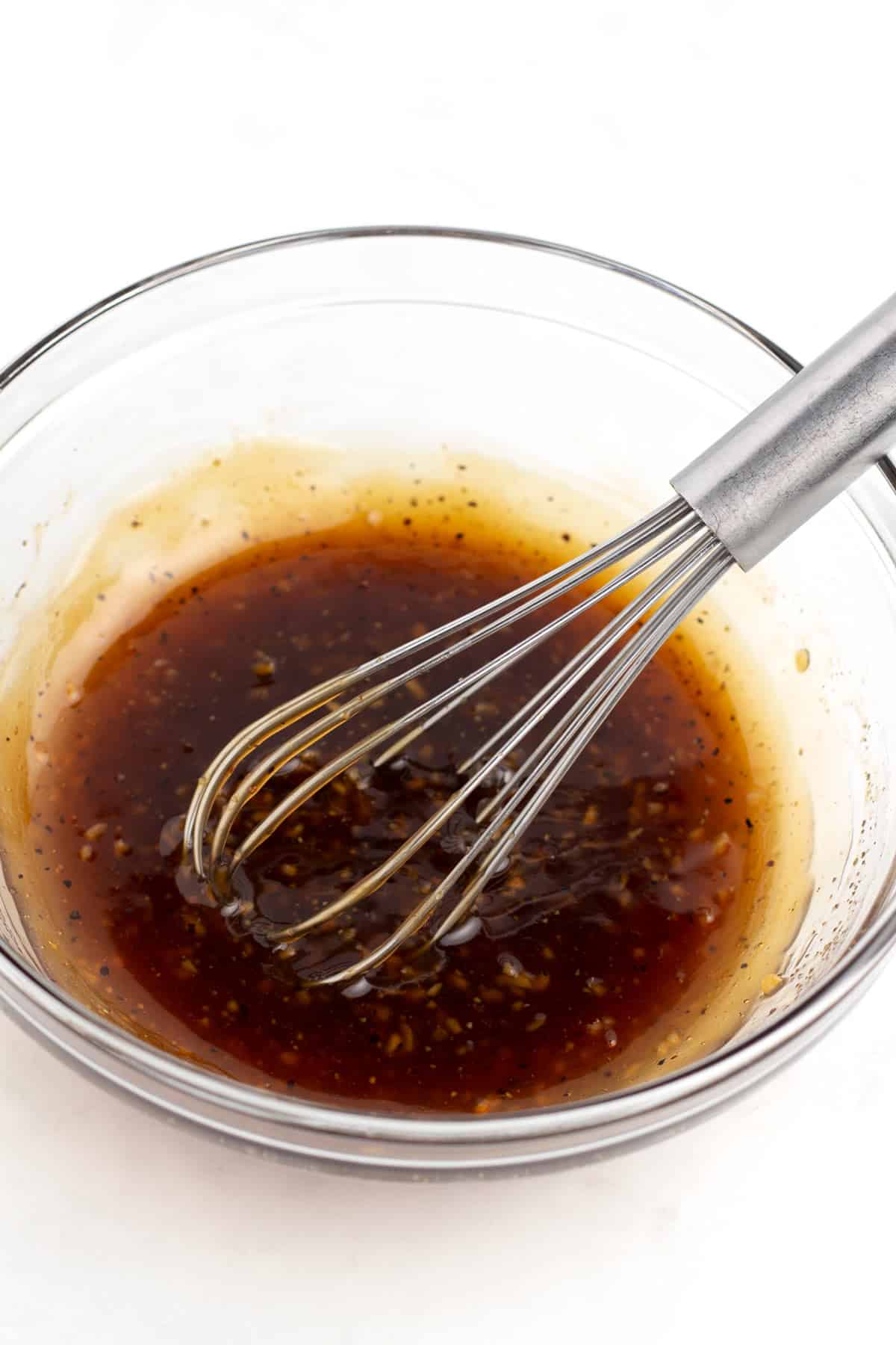 A clear glass bowl full of a dark brown sauce with a whisk sitting in the bowl.