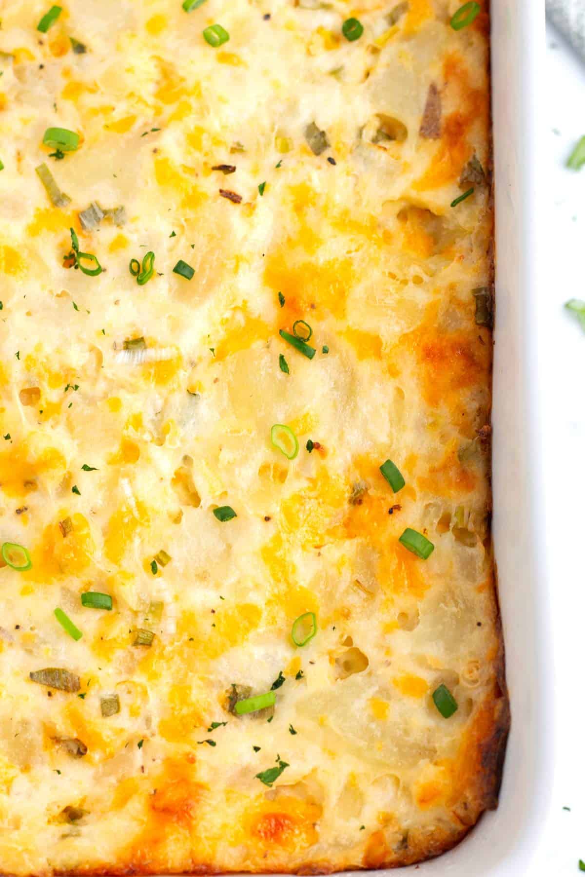 Corner of baking dish filled with sharp cheddar cheese, sour cream, and potatoes baked together.