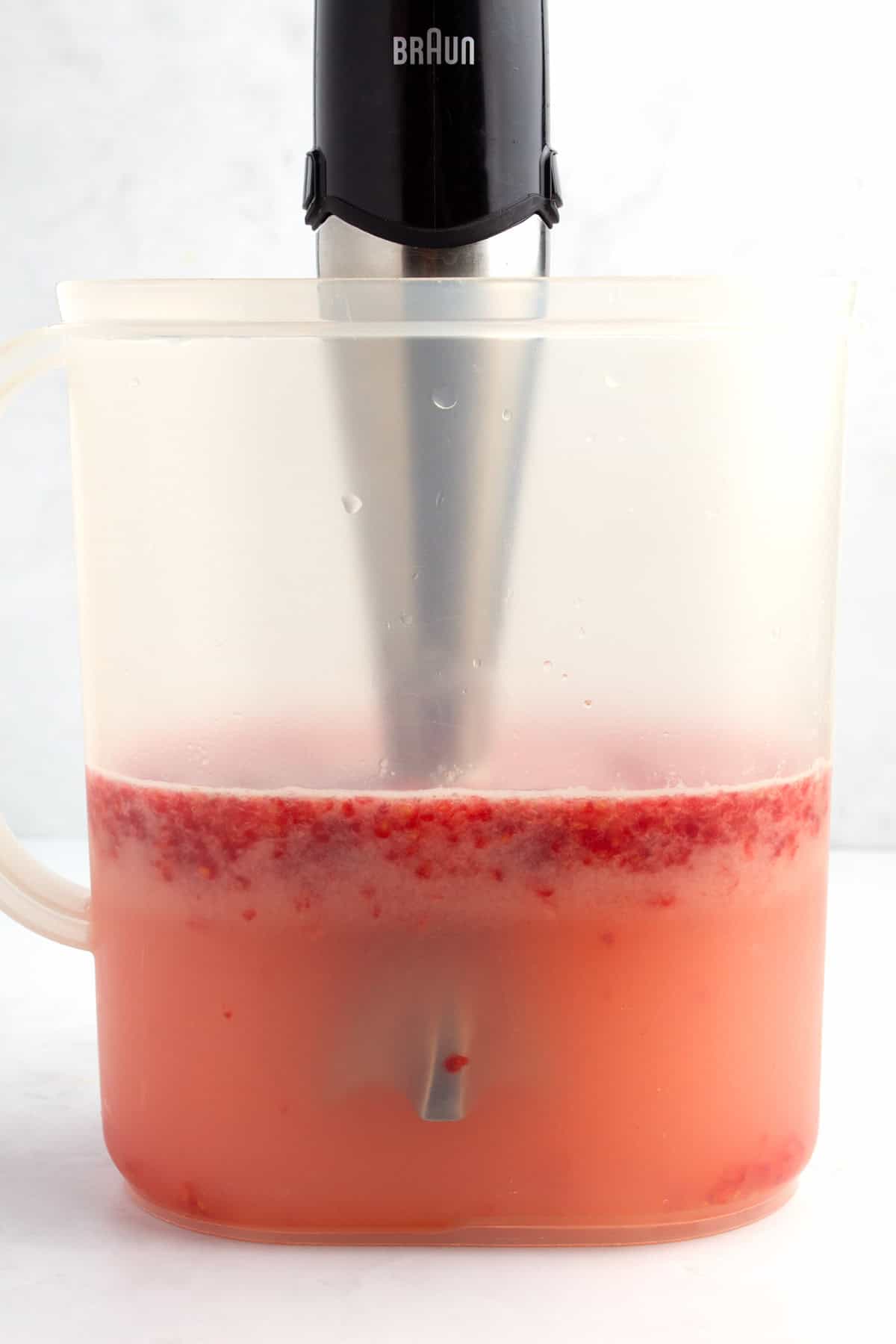 Blending raspberries into pitcher of lemonade.