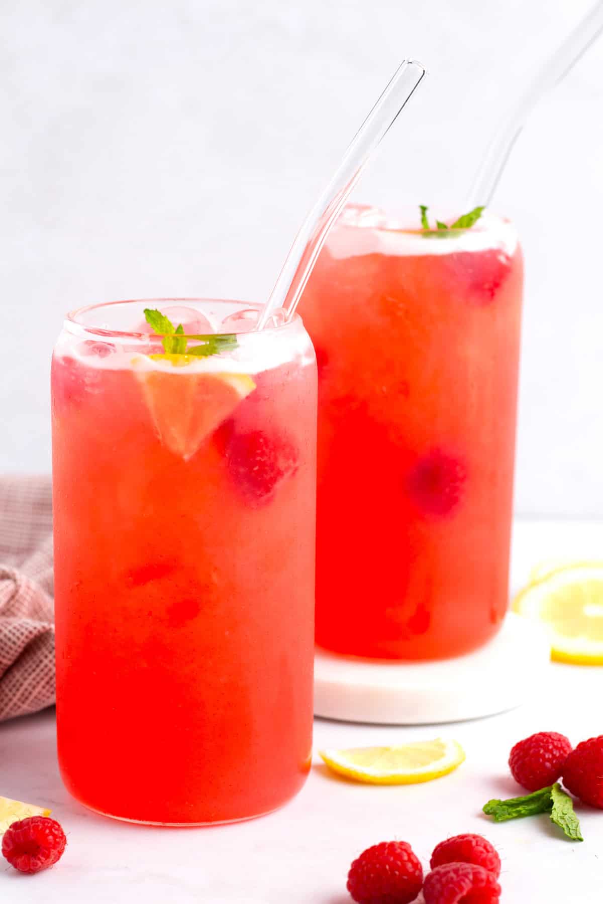 Icy cold raspberry lemonade with mint sprig and napkin on tabletop.