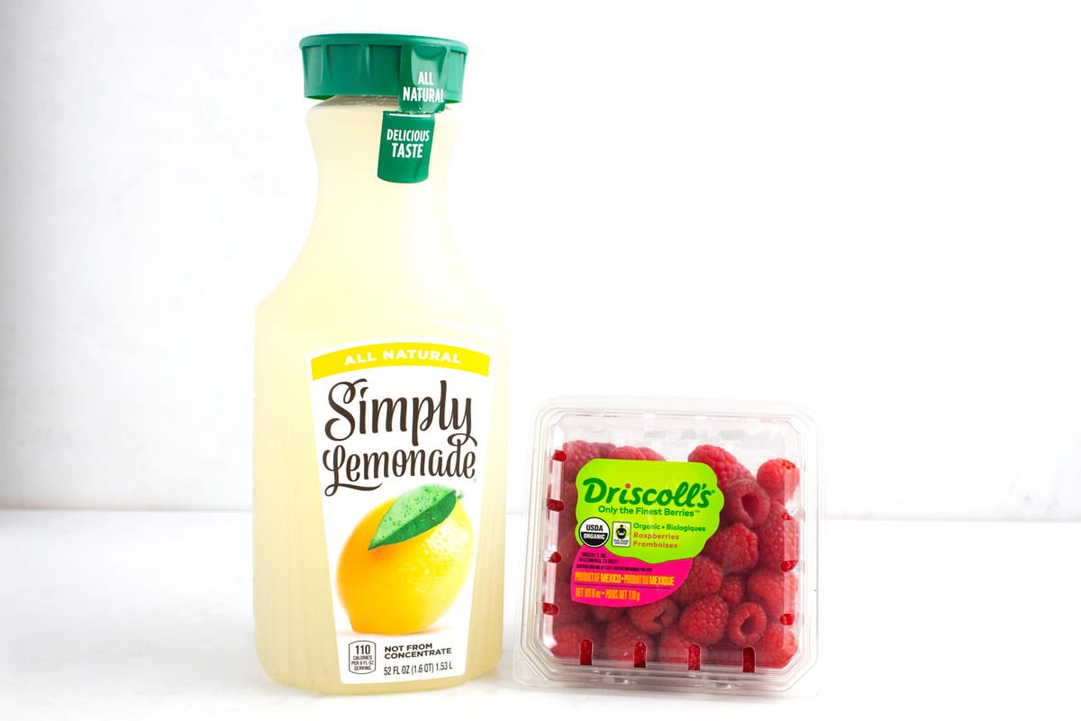 Container of lemonade and package of fresh raspberries on counter.