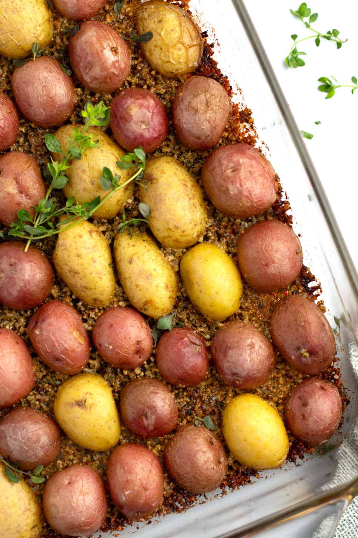 Fresh thyme sprigs on oven roasted parmesan potatoes in pan with green towel.