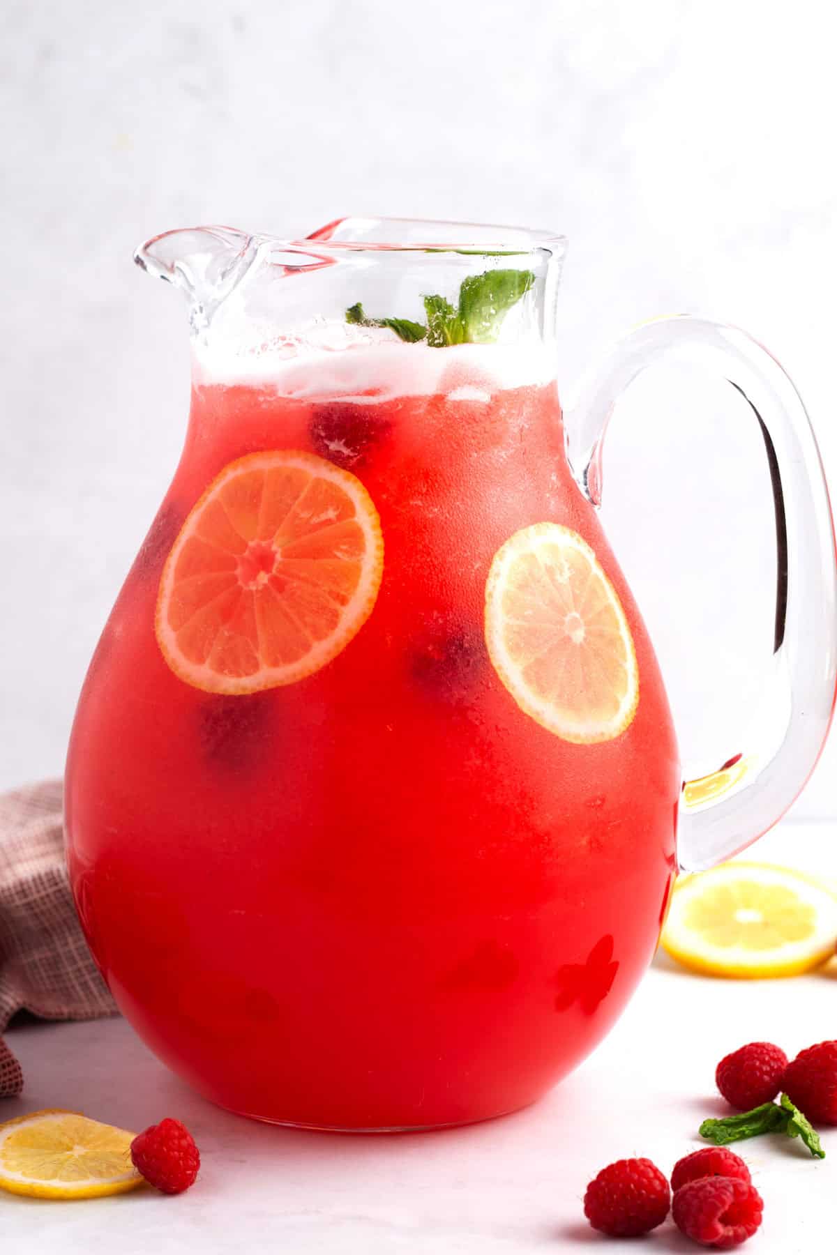 Pitcher filled with raspberry lemonade alongside floating lemon slices and fresh berries.