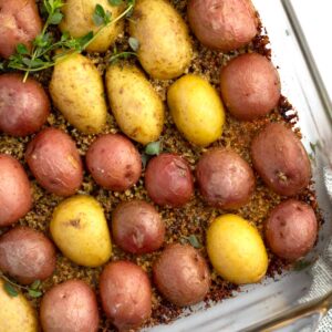 Corner of glass baking dish with crusted parmesan potatoes and sprigs of thyme.