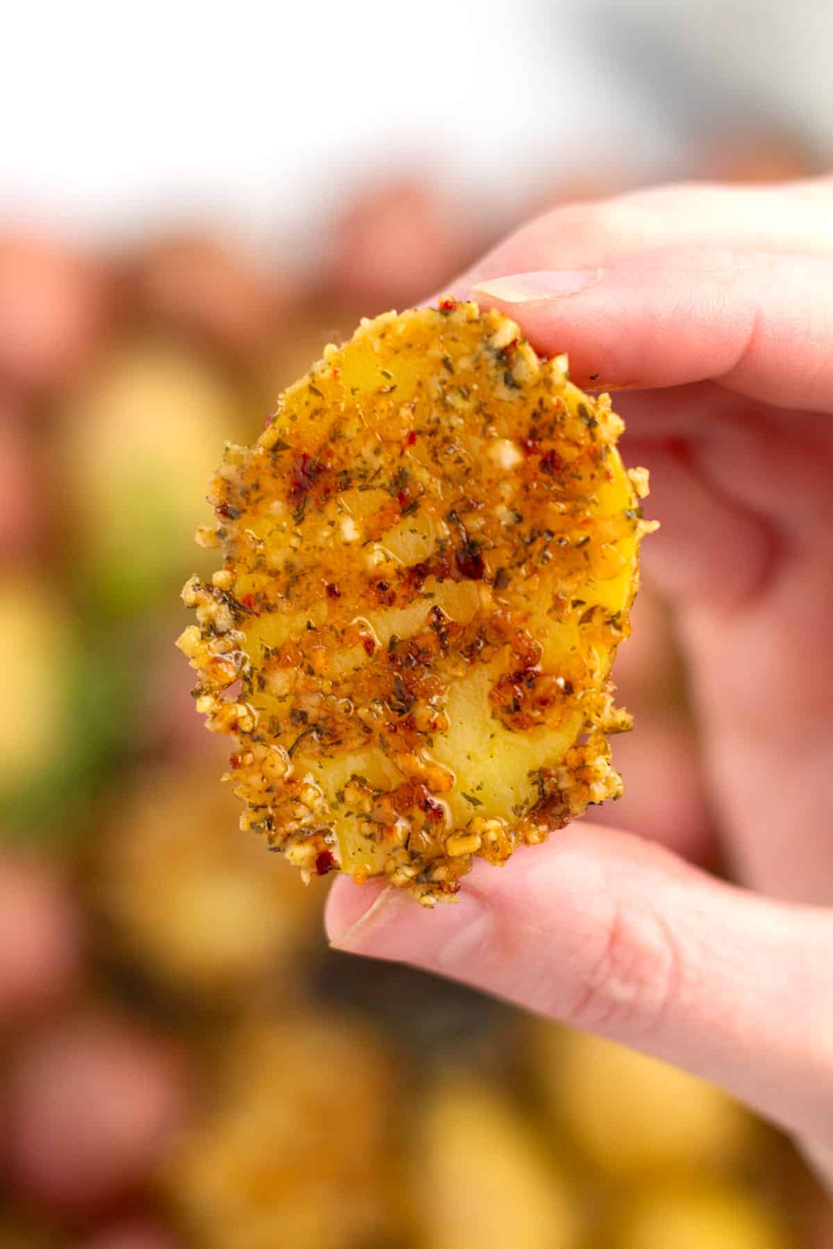 Up close parmesan coated potato being held above pan of baking dish.