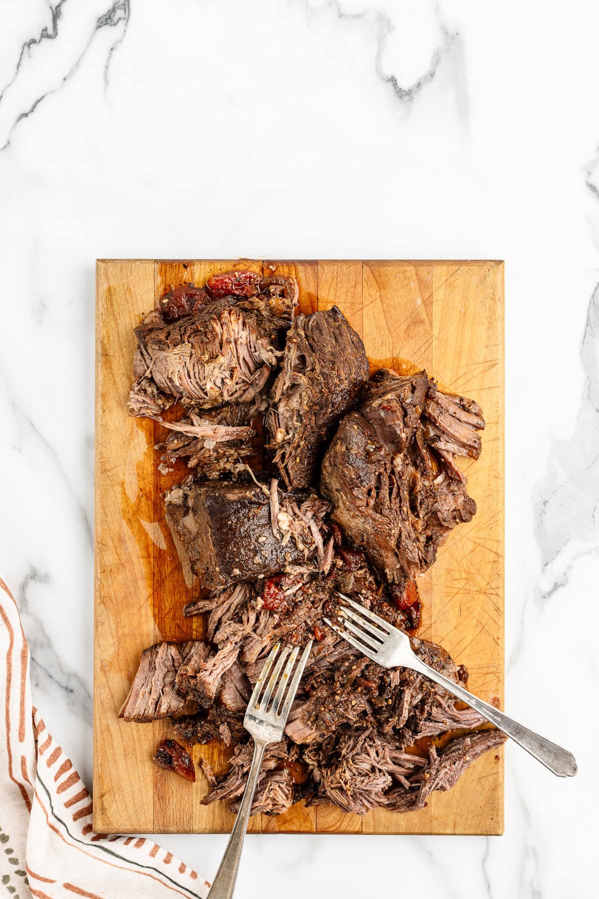 Two forks resting on top of a pile of pulled beef on a wooden cutting.