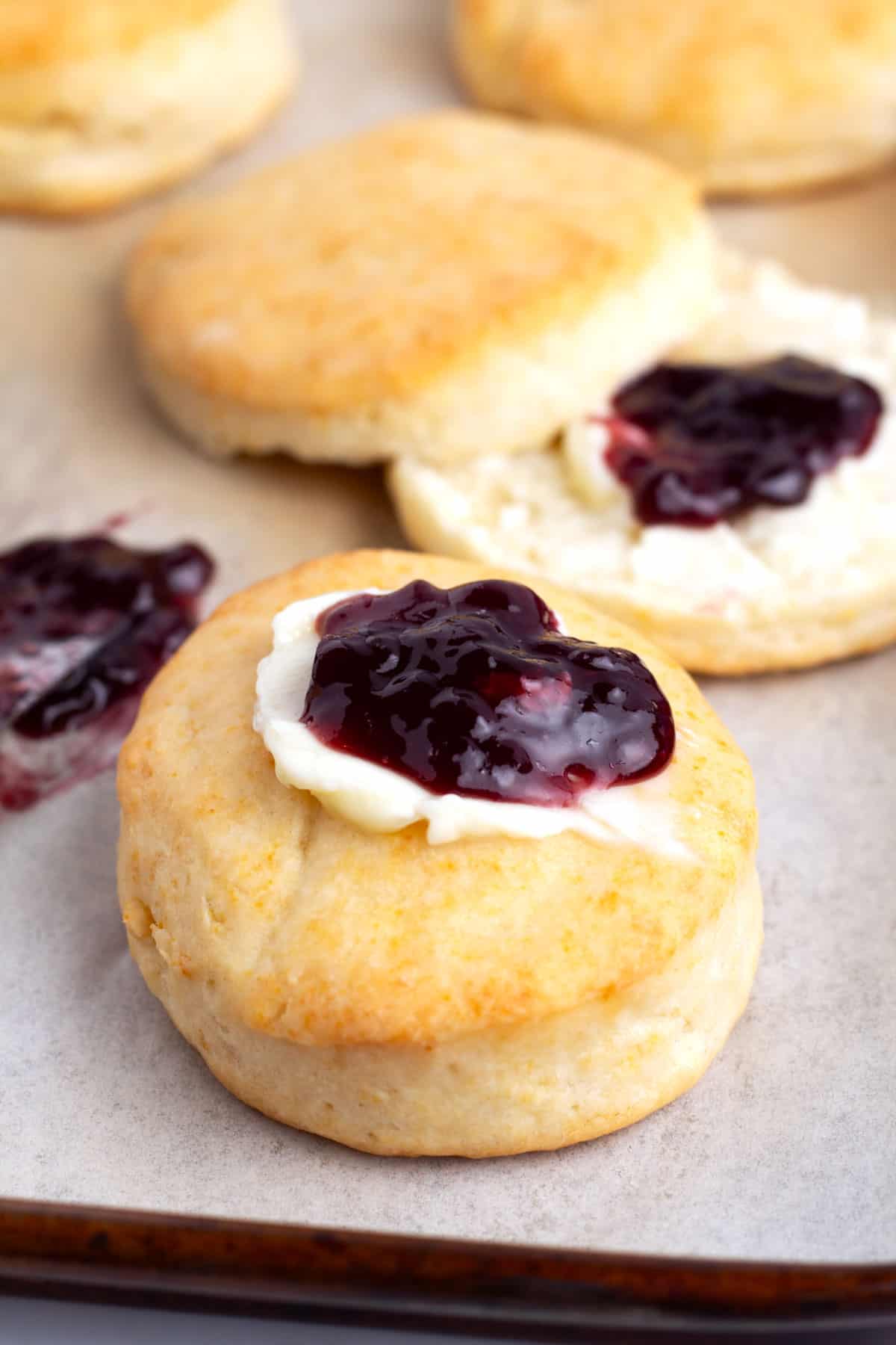Four cream biscuits on a sheet pan topped with butter and blackberry jelly.