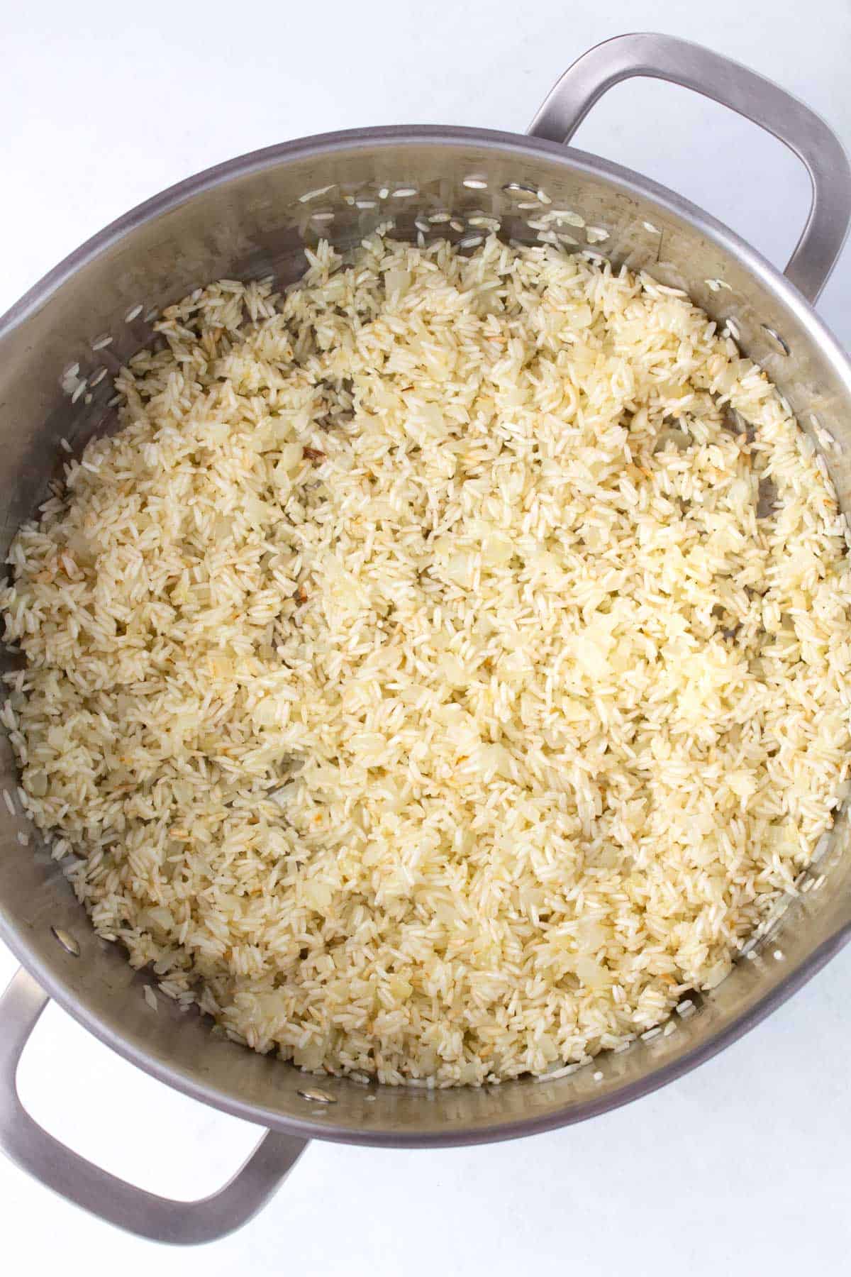 Step two of making Mexican rice by toasting onion and rice in large pot.