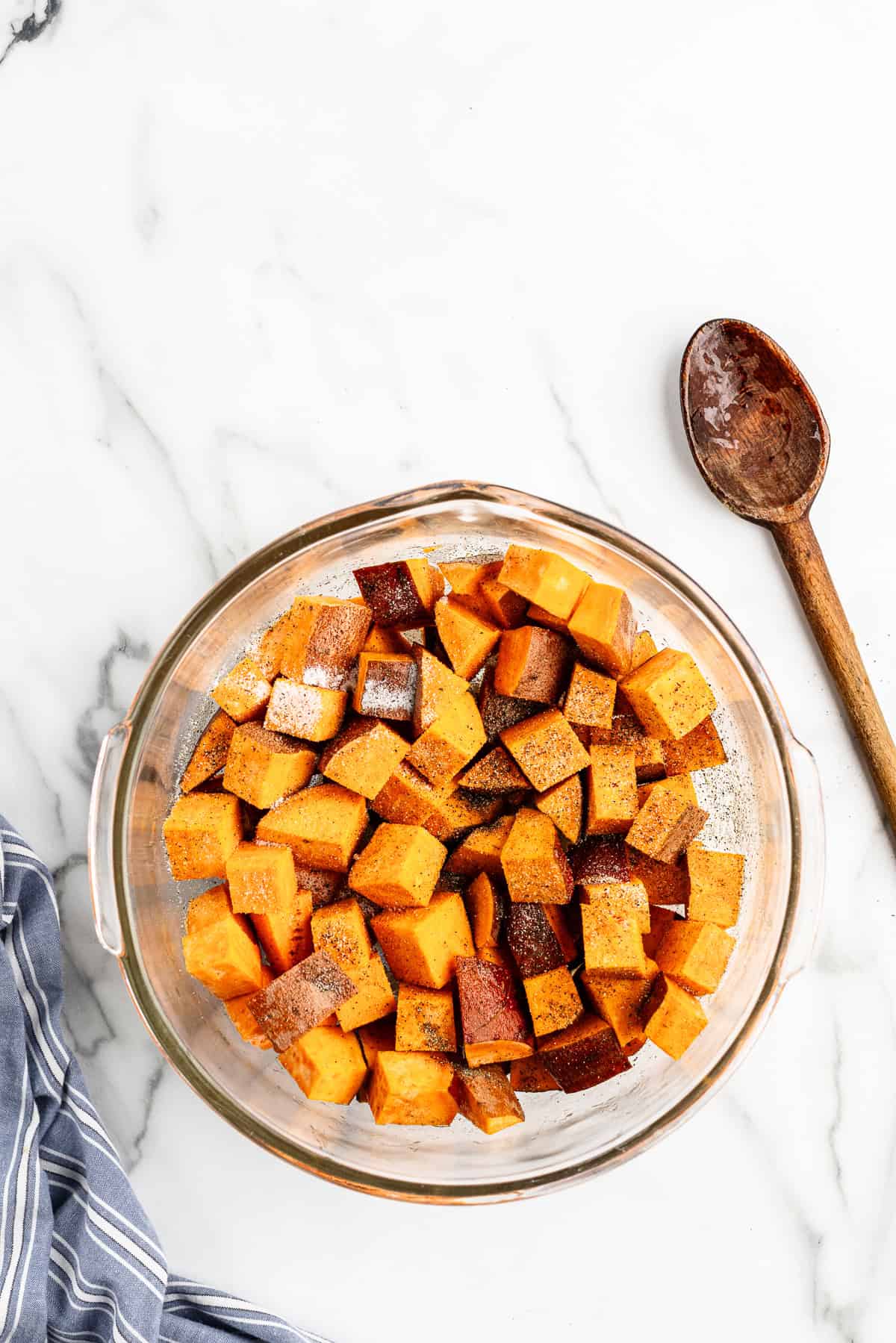 Seasoning cubed sweet potatoes in a bowl.