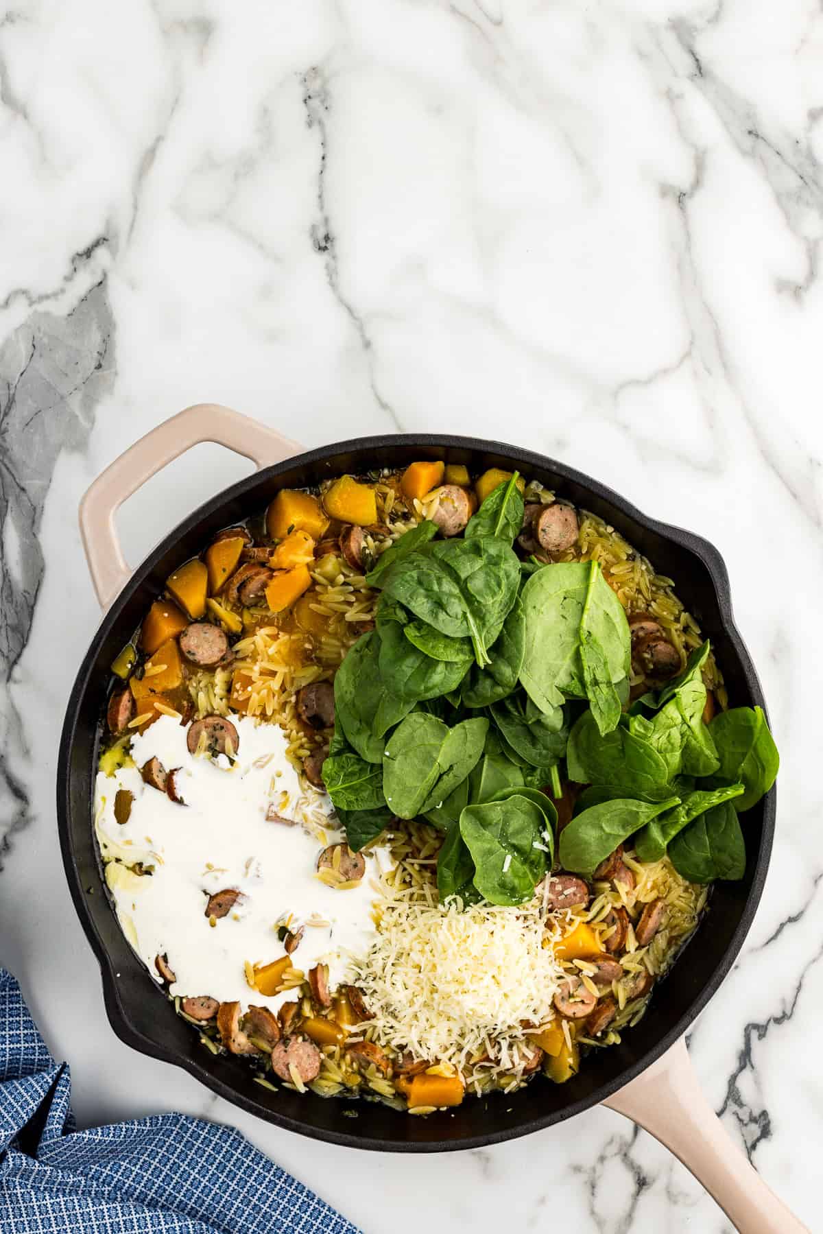 Adding heavy cream, butternut squash, parmesan cheese, and spinach into pasta.