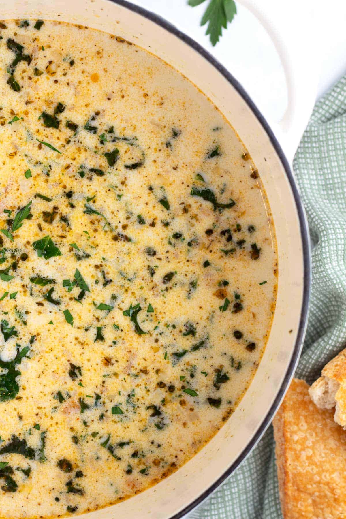 Finished pot of potato, sausage, and kale soup with napkin and french bread.