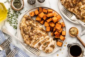 Overhead view of plated sheet pan dinner of chicken breasts in maple sauce with side dish of sweet potatoes.