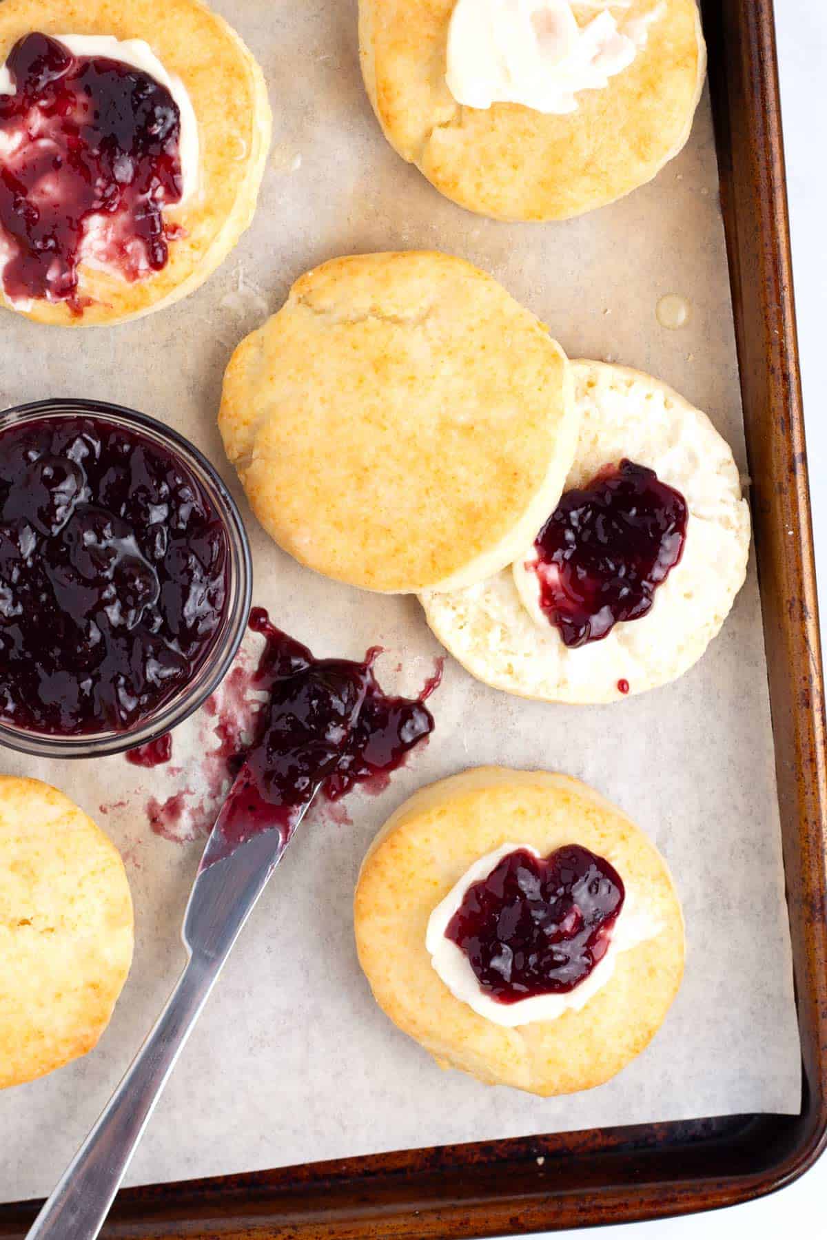 Parchment paper lined baking sheet with biscuits with butter and jam.