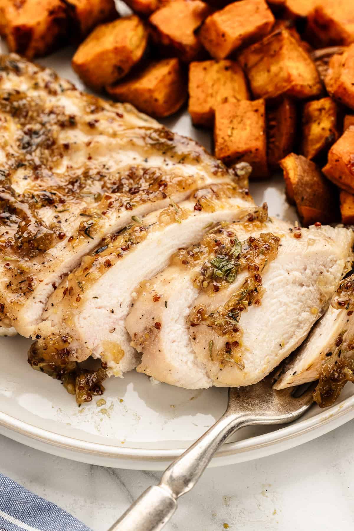 Fork on a dinner plate with slices of chicken and sweet potatoes.