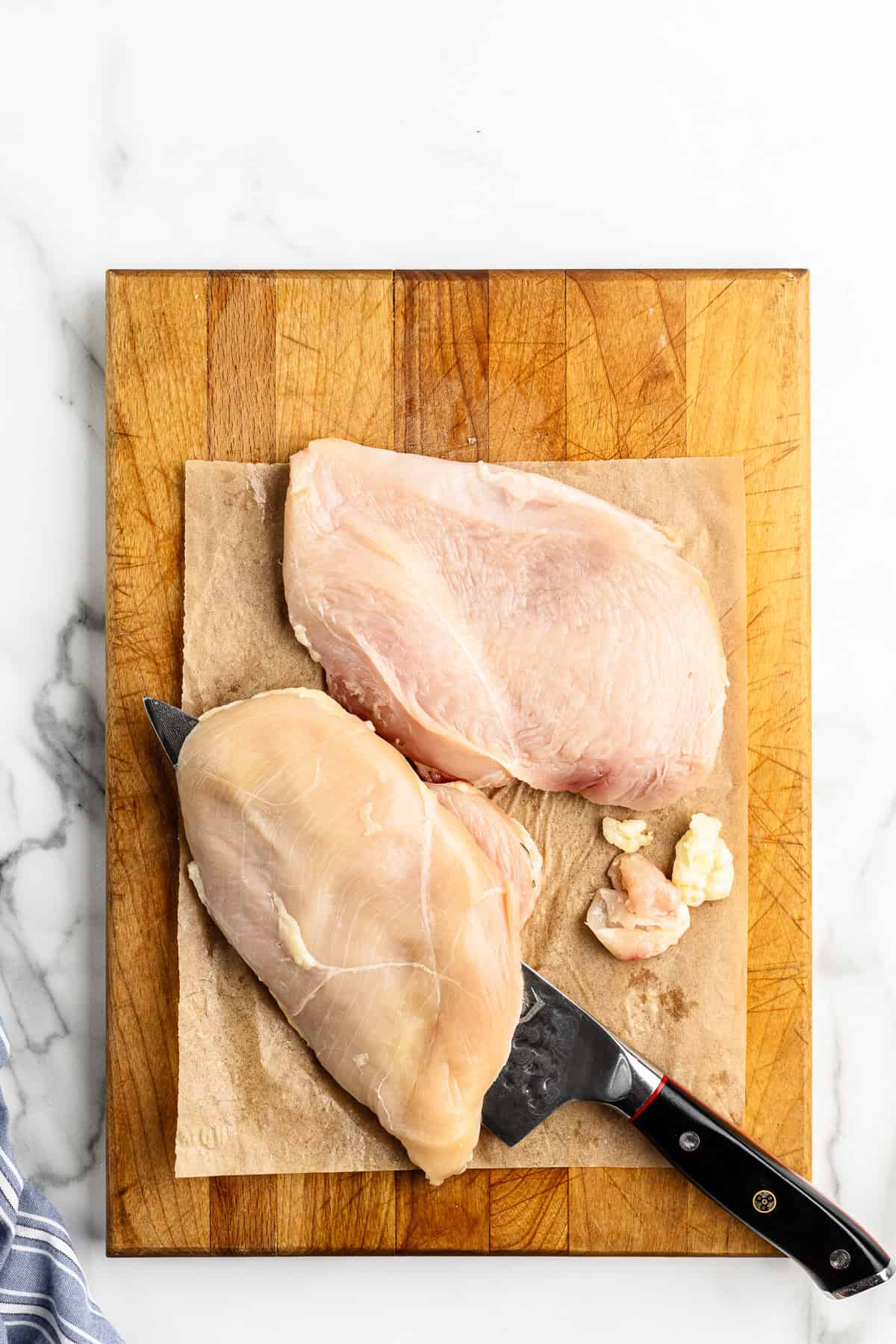 Two chicken breasts on a cutting board cut in half and trimmed of fat.