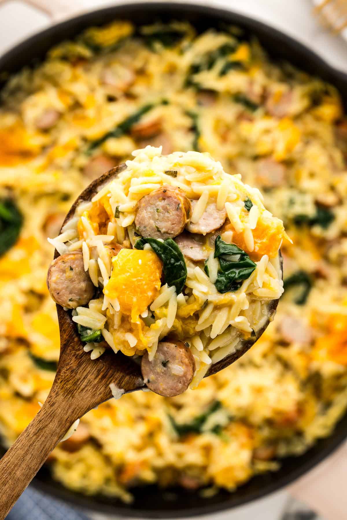 Up close wooden spoon with butternut squash, chicken sausage pasta.