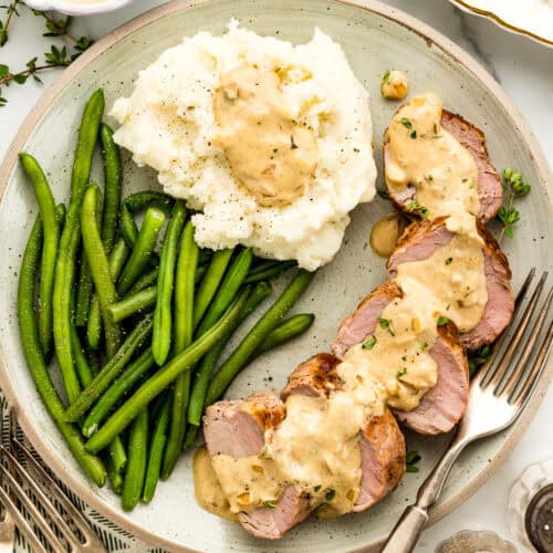 Dinner plate with perfectly cooked pork tenderloin with creamy Boursin sauce with mashed potatoes and green beans.