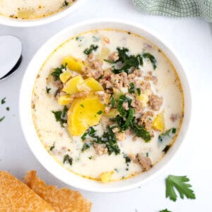 White soup bowl filled with potatoes, sausage, and kale with crusty bread on the side.