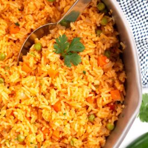 Red mexican rice in serving dish with serving spoon and towel on the side of the bowl.