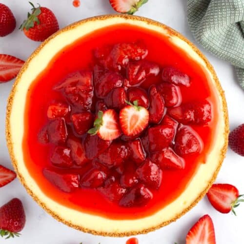 Vibrant red strawberry topping on full cheesecake on cake stand.