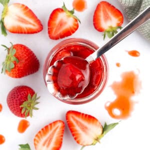 Fresh berries on counter surrounding spoonful of strawberry topping.