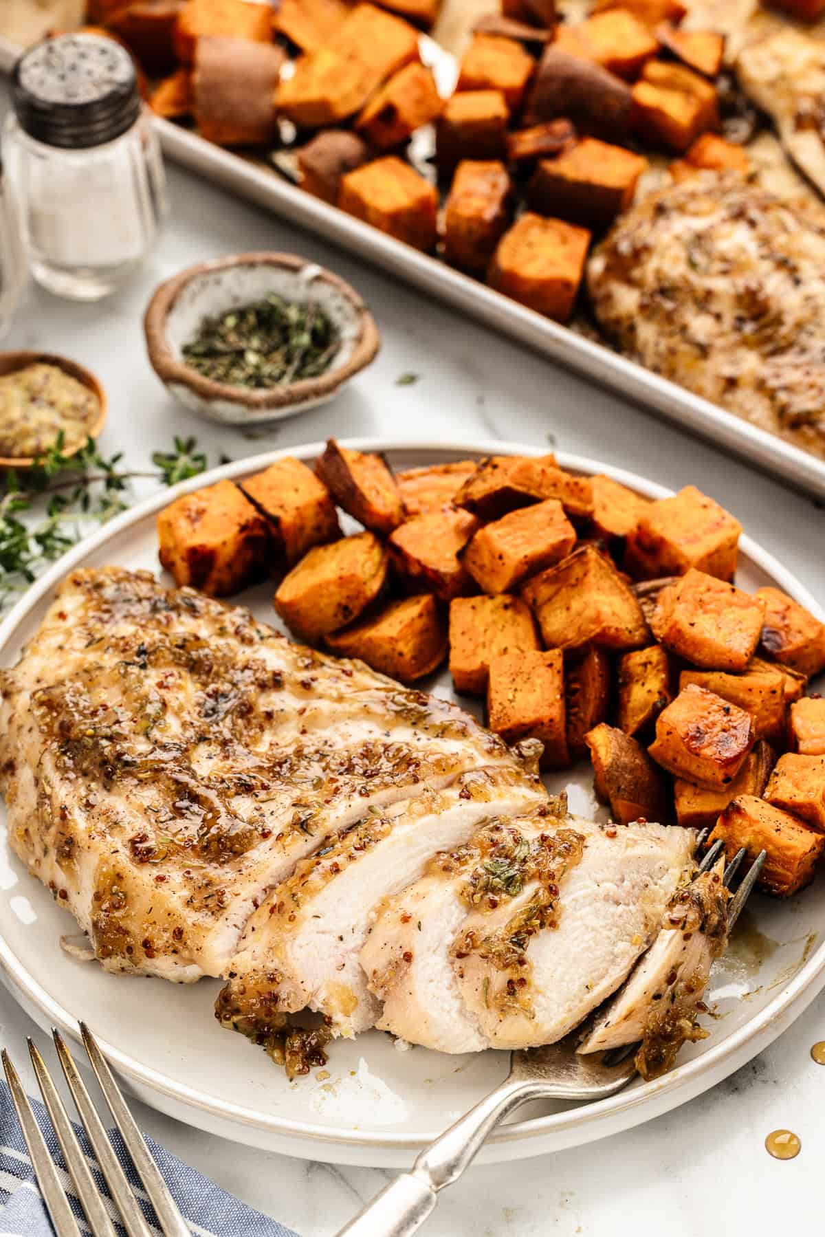 Sheet pan dinner in the background with a plate of chicken and sweet potatoes.