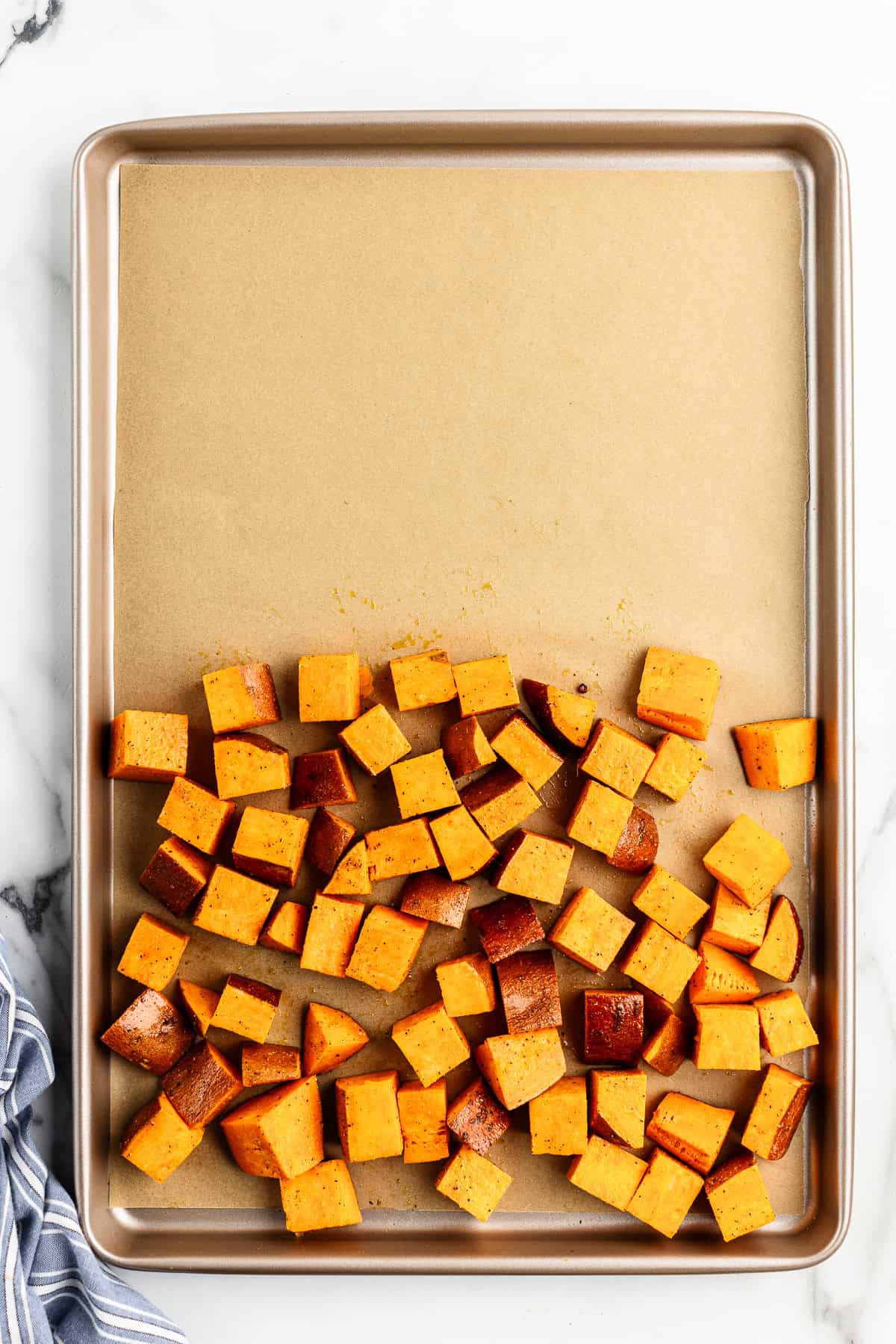 Half of a sheet pan covered with diced, seasoned sweet potatoes.