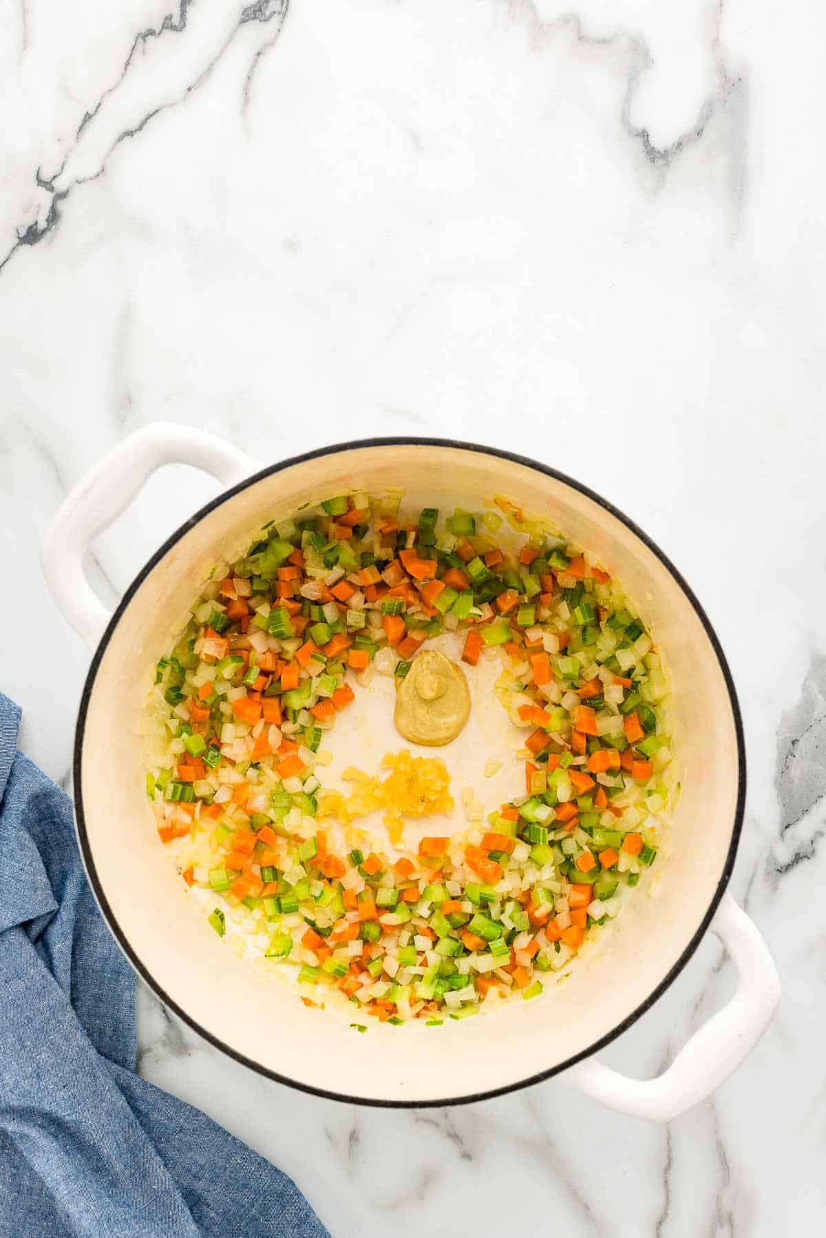 Enameled dutch oven with sautéed vegetables adding in garlic and dijon mustard.