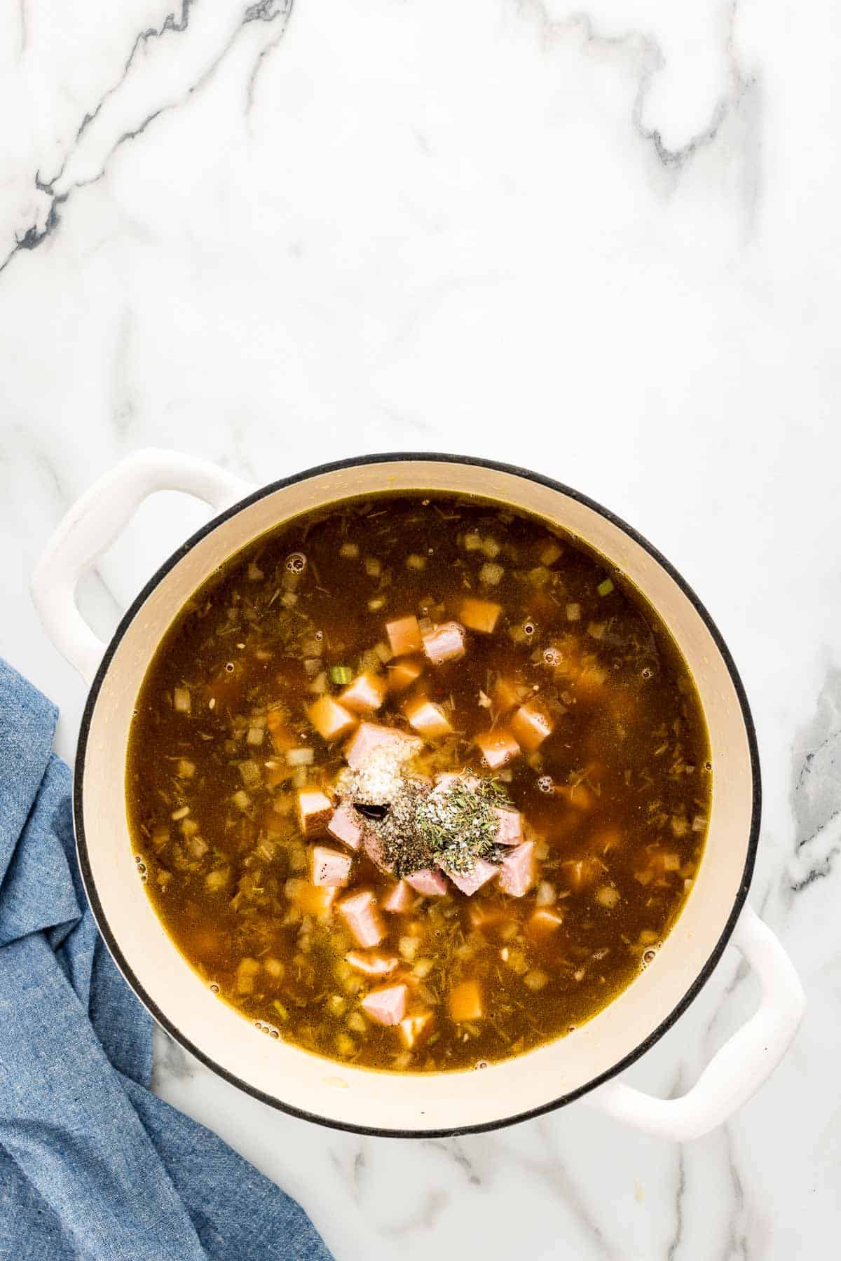 Adding in the seasonings to the potato soup with ham.