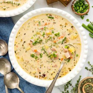 Overhead bowl of soup topped with thyme and green onions with napkin and spoons layered in the background.