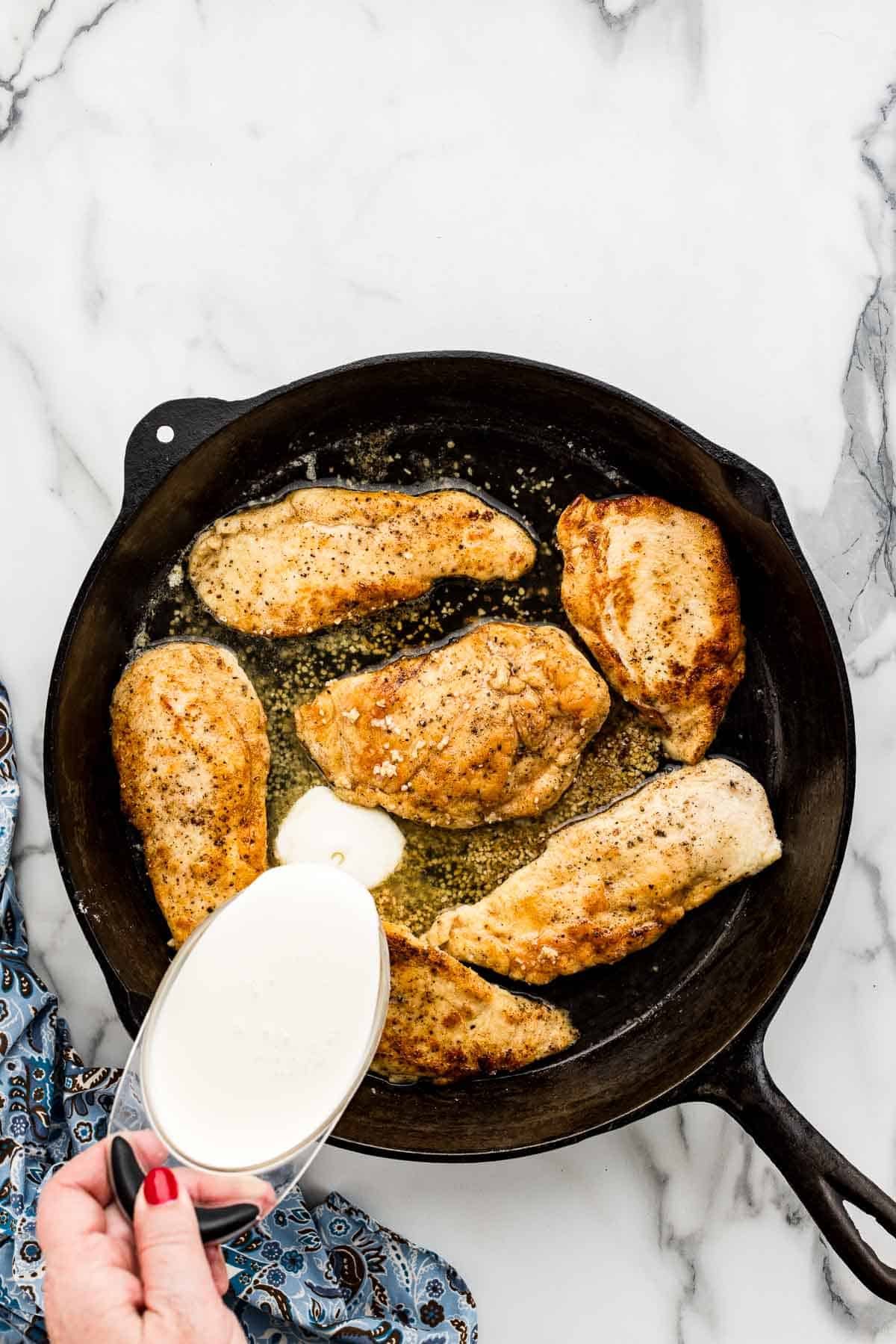 Pouting heavy cream into skillet of garlic chicken.