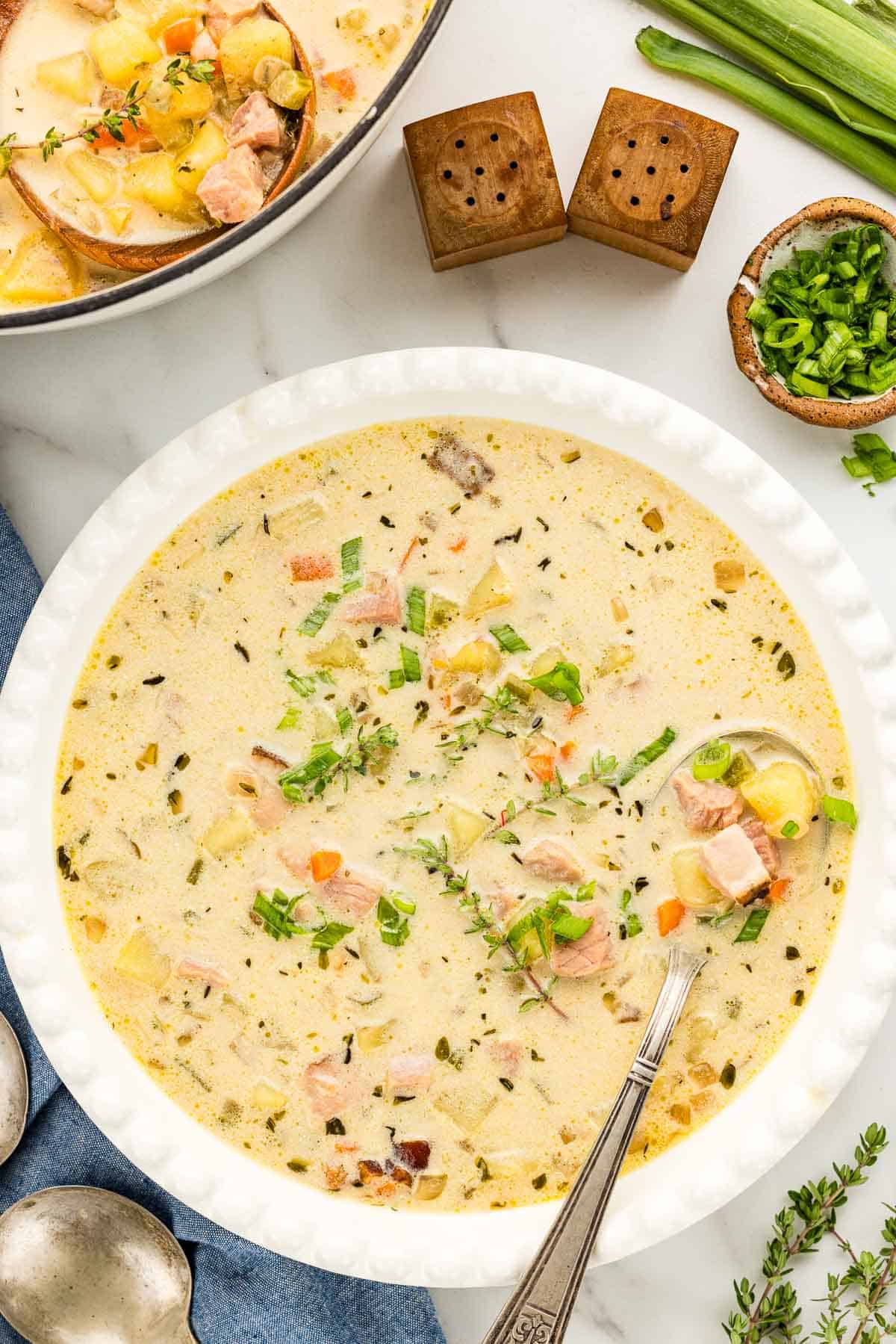 Pot filled with potato and ham soup in the background with bowl full in front topped with thyme.