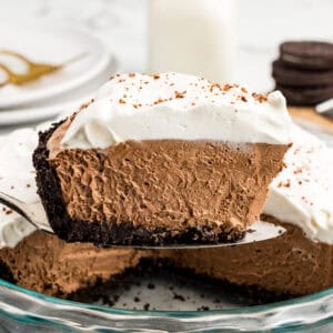 A slice of French Silk pie being lifted out of the pan with Oreos, a glass of milk, and white plates in the background.