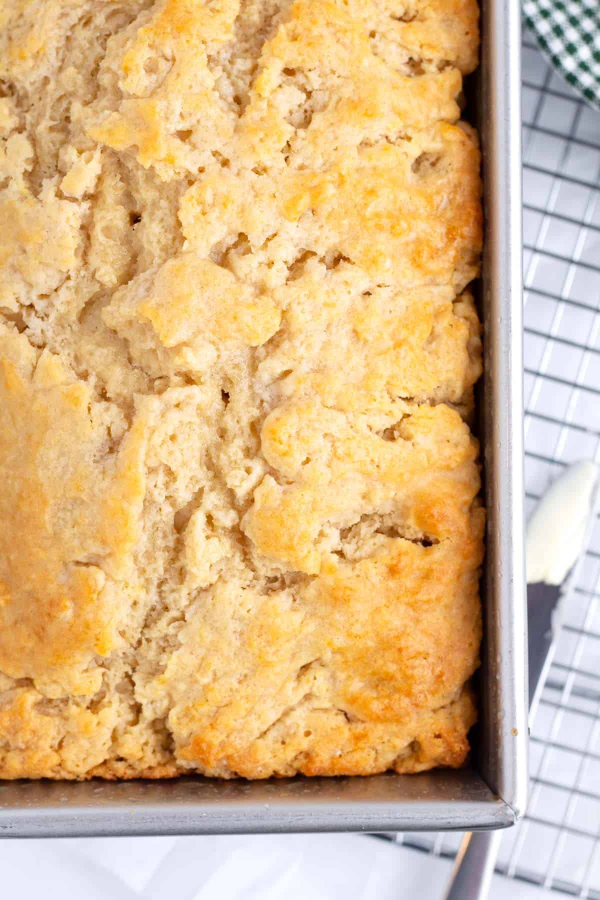 Very close up view of bread with a golden brown, crinkly texture baked in a rectangle pan with a a butter knife on the side.