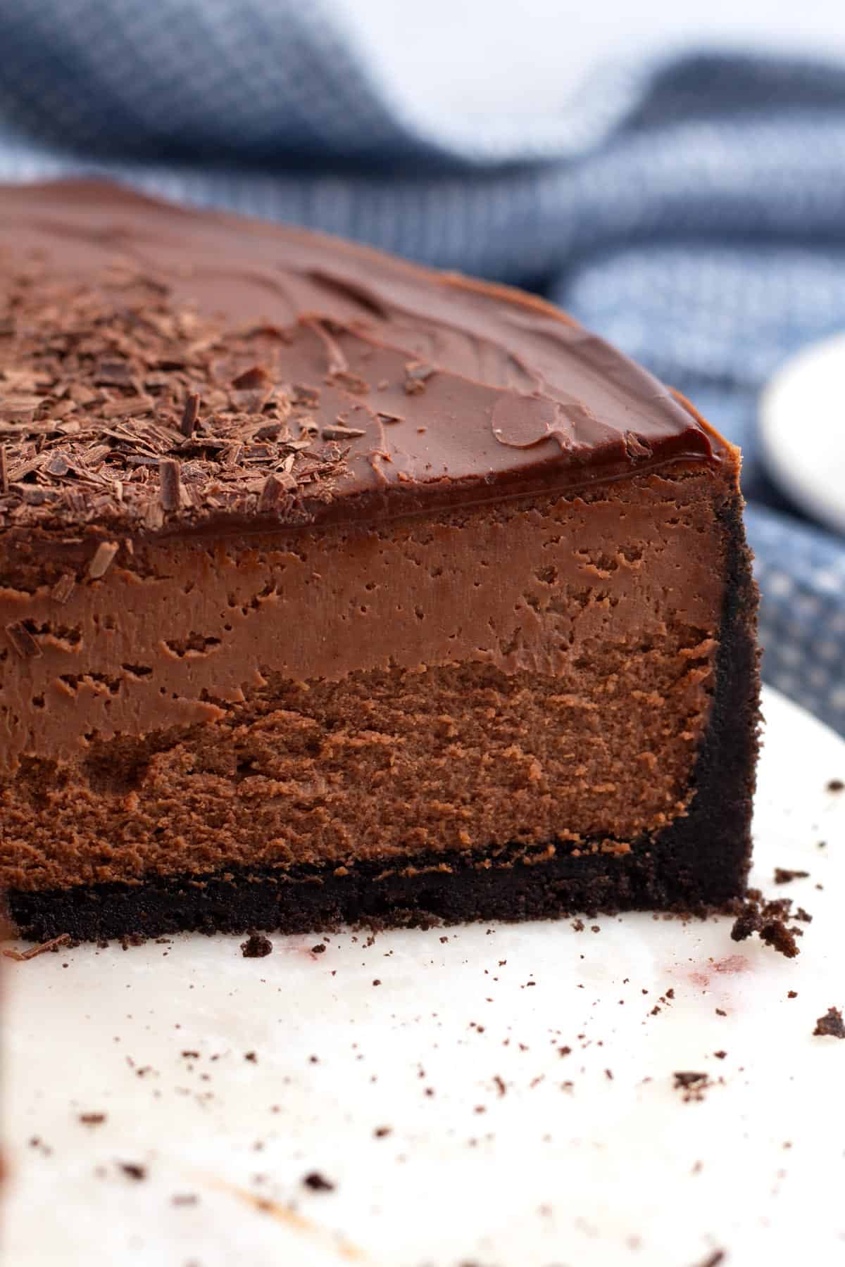 Platter of half of a chocolate cheesecake with a blue and white towel bunched up behind it in the background.