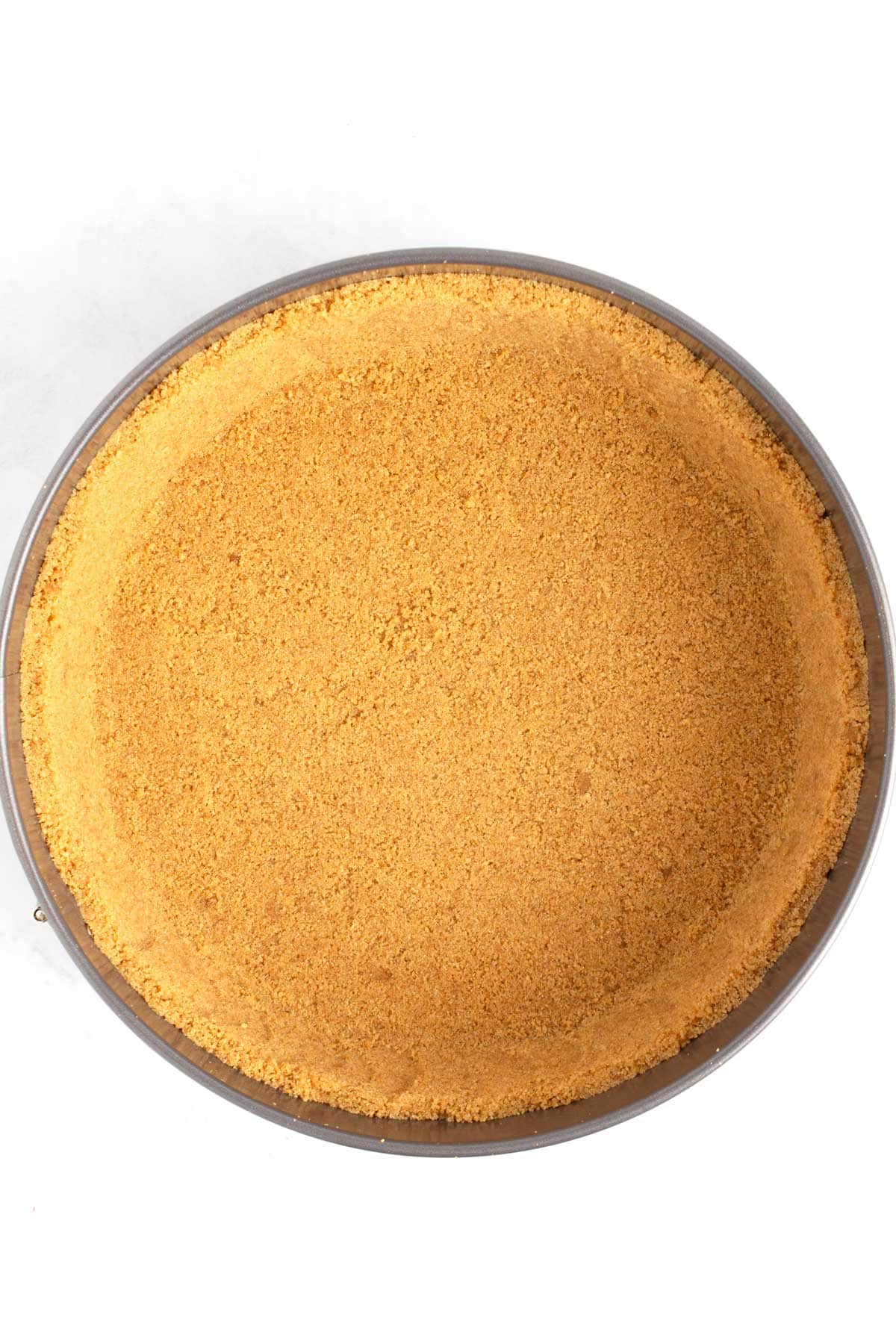 Overhead view of graham cracker crust pressed in and up the sides of cheesecake pan.