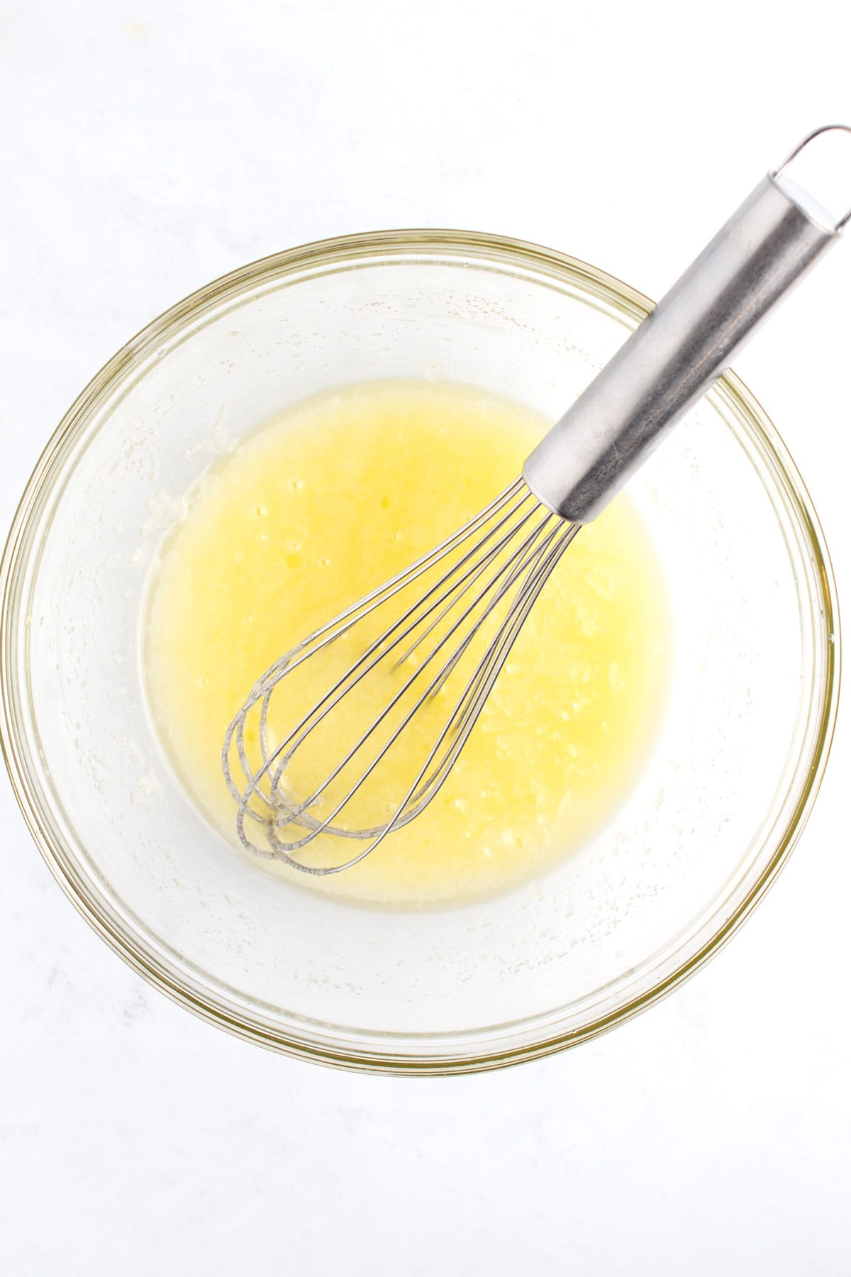 A small glass bowl of melted butter with a whisk sitting in the bowl.