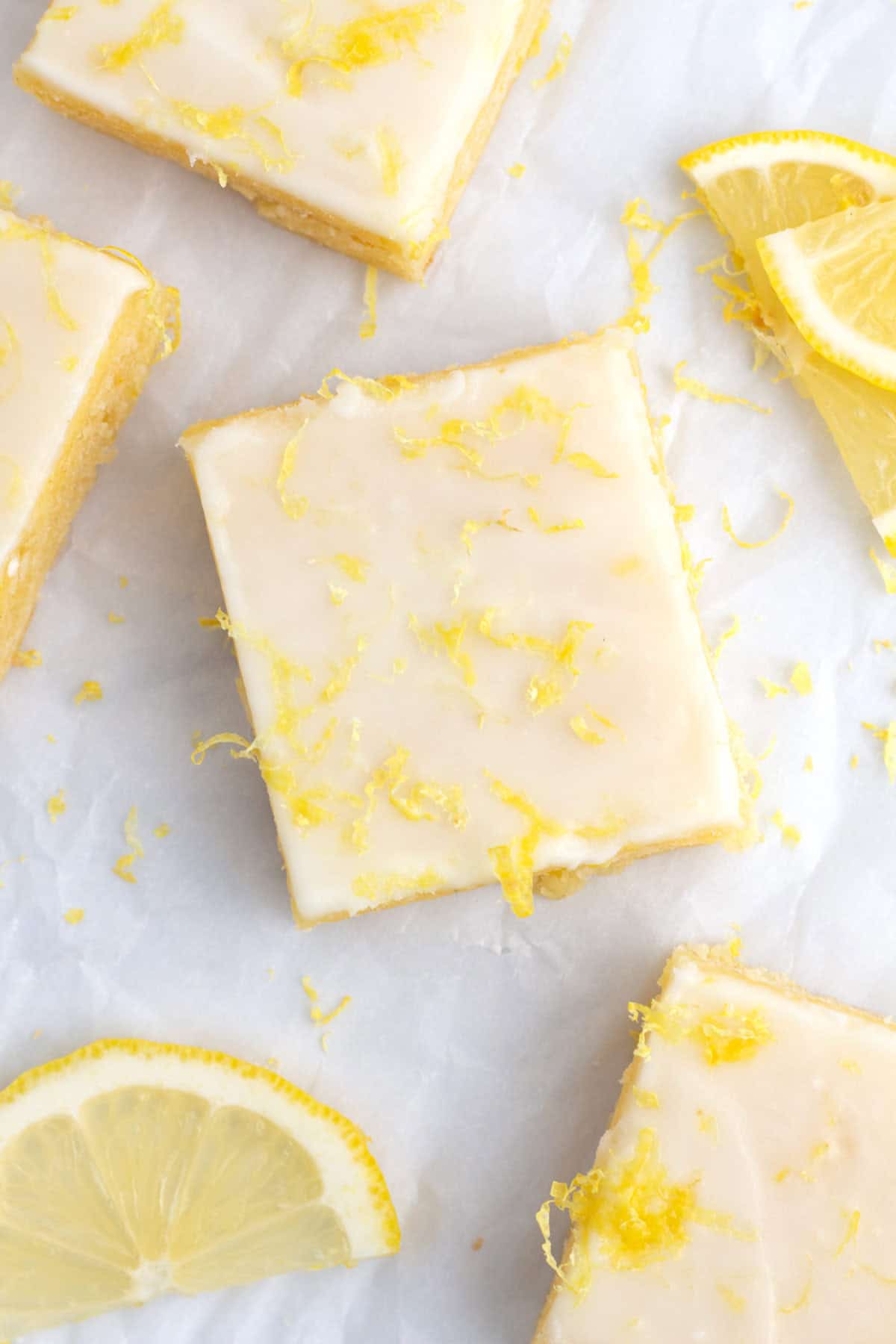 Fudgy lemon brownies covered in lemon glazed and topped with zest staggered on paper.
