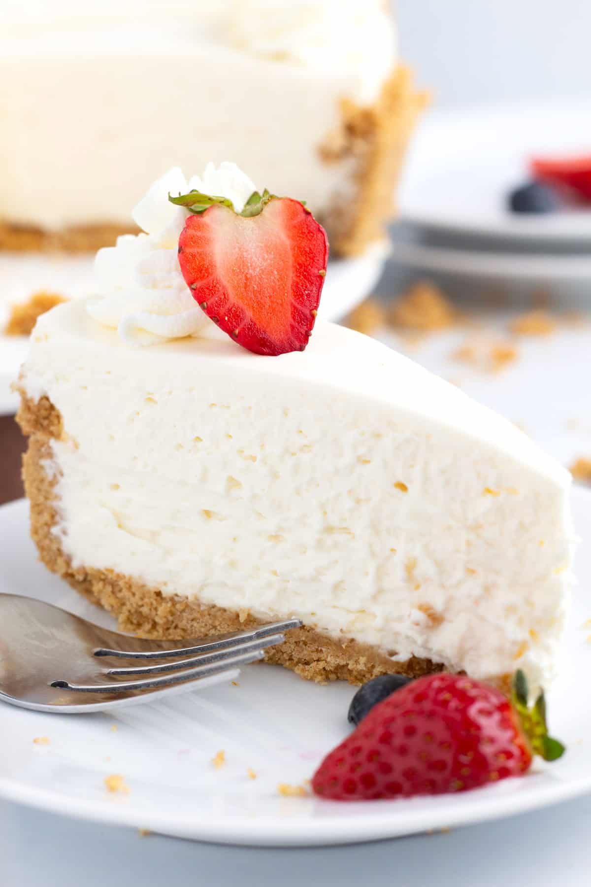 Dessert plate with piece of light and creamy no bake cheesecake topped with strawberry for garnish.