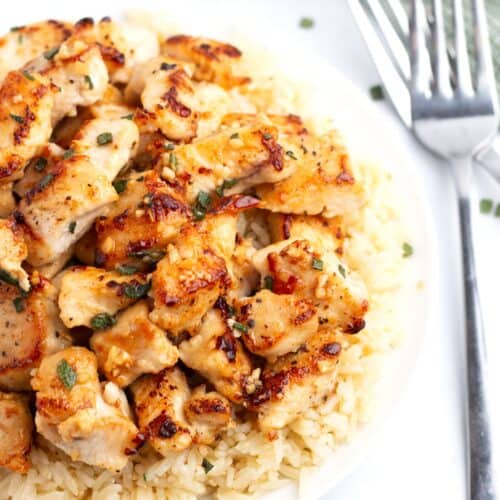 Brown chicken pieces coated in glossy butter, garlic, and sage on top of rice with two forks next to the plate.