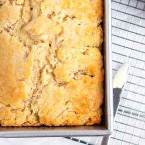 An overhead view of a silver loaf pan of golden, crinkly bread on top of a wire rack with a small butter knife on the right side of the pan.