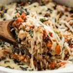 A really close up view of a spoon lifting a cheesy Italian casserole sprinkled with basil.