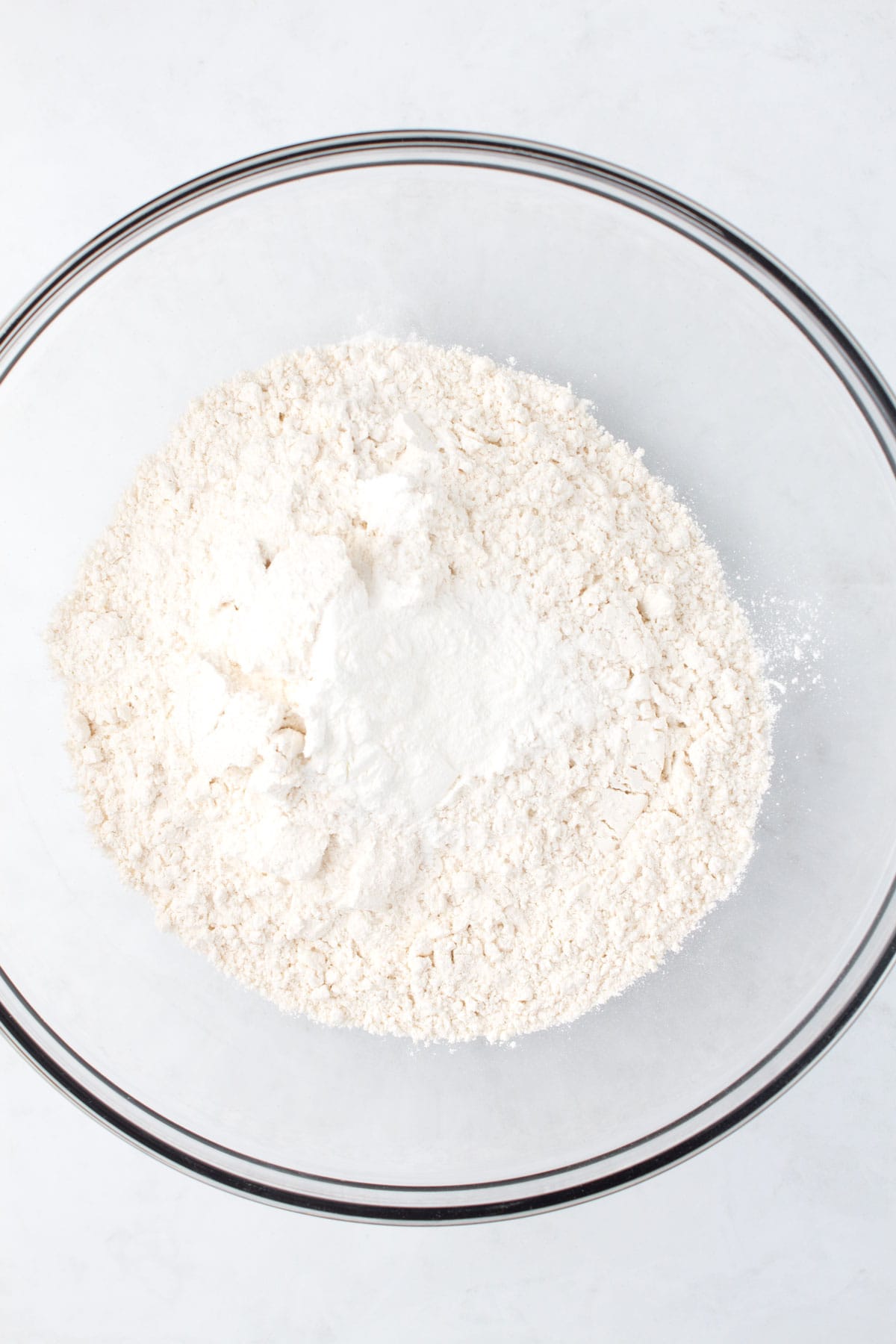 A clear glass bowl of flour and baking powder.