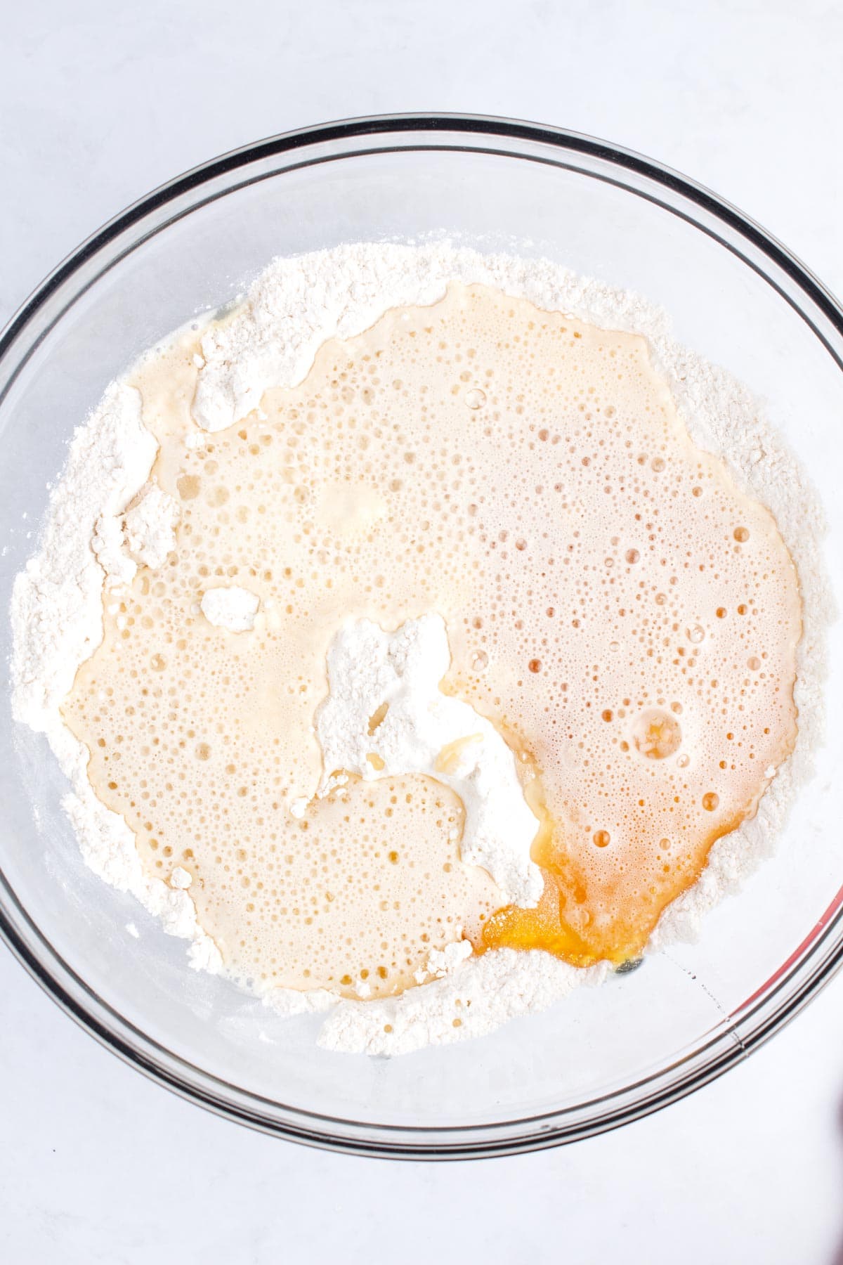 A clear glass bowl with fizzy liquid and honey poured on top of white flour.
