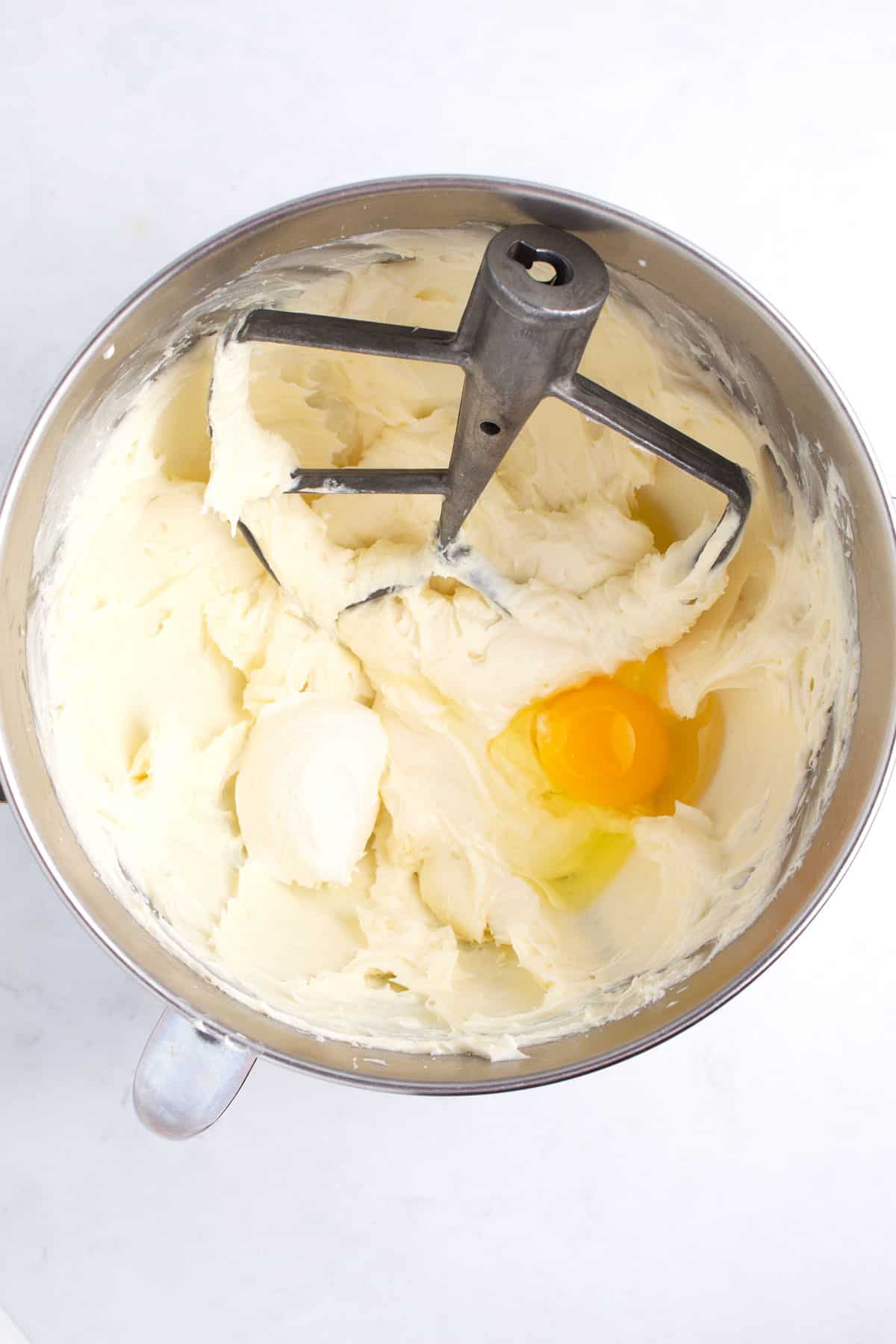 Stainless steel bowl with frosting and unblended eggs in it with a stand mixer paddle in the bowl.