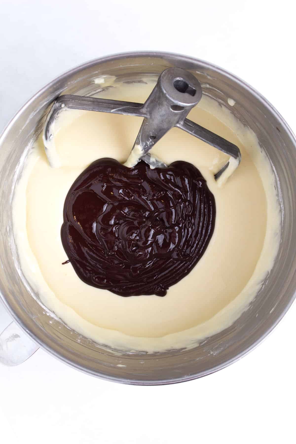 Stainless steel bowl with batter and melted chocolate in it and a stand mixer paddle in the top part of the bowl.